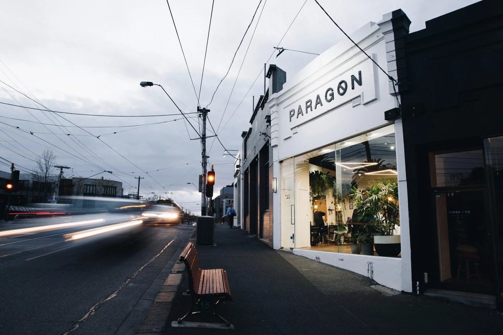 Paragon Studio's white shopfront on High Street, Armadale, at dusk with tram lights passing